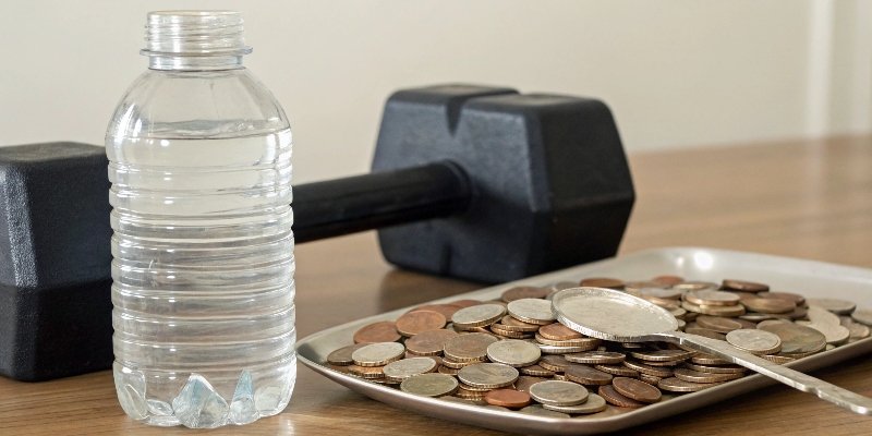 A 500ml bottle of water next to a pile of coins and a tablespoon.