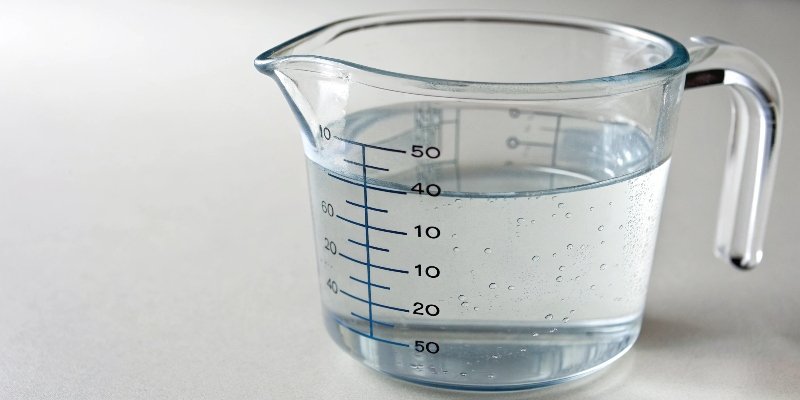 A kitchen measuring cup filled to the 100ml line with water.