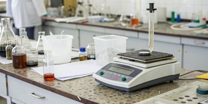 A modern laboratory balance displaying an unstable reading amid a cluttered lab environment.