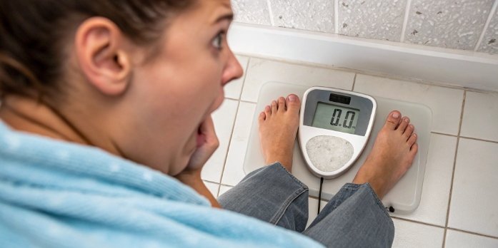 A person looking down at a digital bathroom scale with a surprised expression