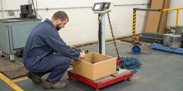 Calibration vs. Replacement of Weighing Scales A technician calibrating an industrial scale next to a new weighing scale in a box.