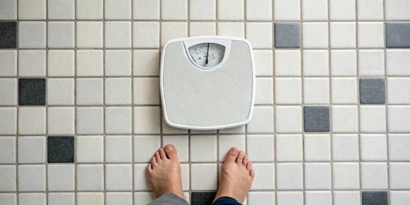 An overhead view of a modern digital bathroom scale on a tiled floor.