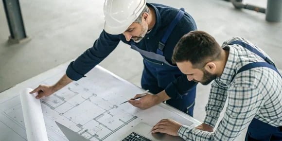 Industrial Scale Partnership A software developer and a hardware engineer collaborating over a blueprint of an industrial scale.