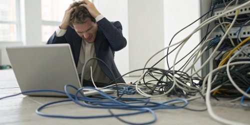 A tangled mess of cables connected to a frustrated business person looking at a computer screen with an error message