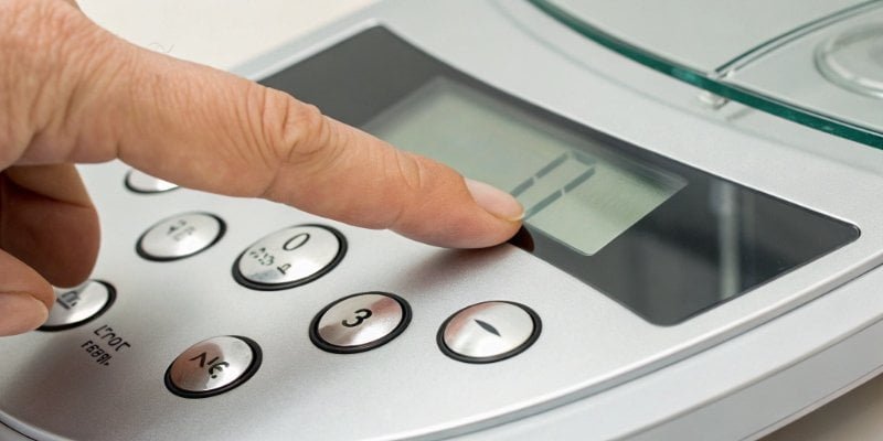 A close-up of a finger pressing the 'TARE' button on a digital scale's control panel.