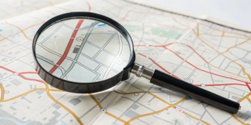 A magnifying glass hovering over a map pointing to a factory location.