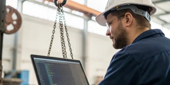 Evaluating Manufacturer's Tech An engineer examining code on a computer screen with an industrial scale in the background.