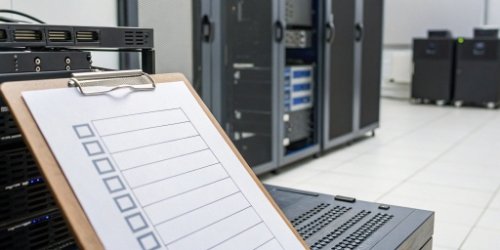 A checklist on a clipboard with hardware and software components next to it.