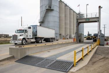 A large truck driving onto a weighbridge platform at a grain silo facility.