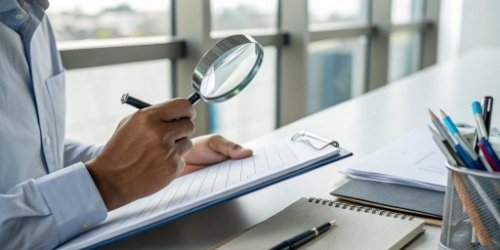 A person using a magnifying glass to inspect a checklist for a project plan.