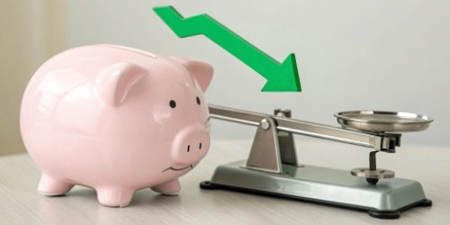 Reducing Production Costs A piggy bank next to an industrial scale with a green arrow pointing down.