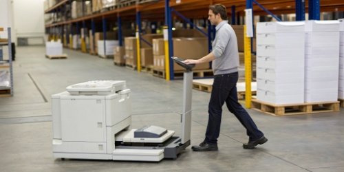 An operator walking between a weighing scale and a separate printer in a warehouse setting