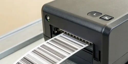 A close-up shot of a high-speed thermal printer head producing a clear, scannable barcode label.