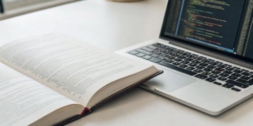 An open book of technical documentation next to a laptop displaying code