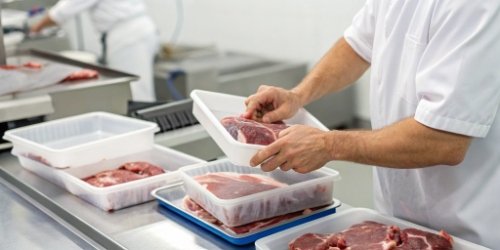 A worker applying a freshly printed label to a package of meat