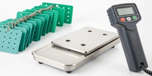 An assortment of EID ear tags, a handheld RFID reader, and a stainless steel industrial scale.