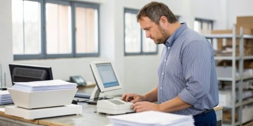 A purchasing manager comparing datasheets for two different weighing terminals at a desk.