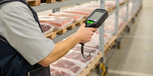 A warehouse worker scanning a barcode on a meat package with a handheld device, with a green checkmark on the screen.