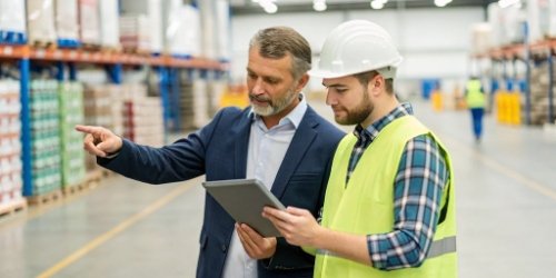 A manager and a warehouse worker looking at a tablet, planning warehouse layout and stacking rules.