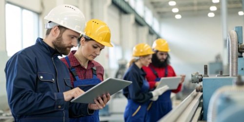 A team of factory workers in a training session using tablets and industrial machinery