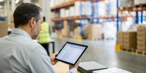 Masking Customer Data for Secure Supplier Sorting A logistics manager reviewing data on a tablet in a warehouse, with blurred out customer names.