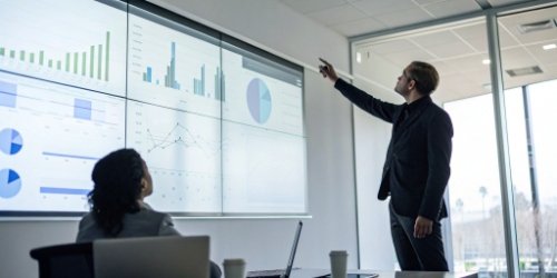 A manager pointing at a data projection screen showing sorting analytics